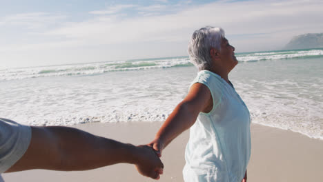 una pareja de ancianos afroamericanos caminando y tomados de la mano en la playa