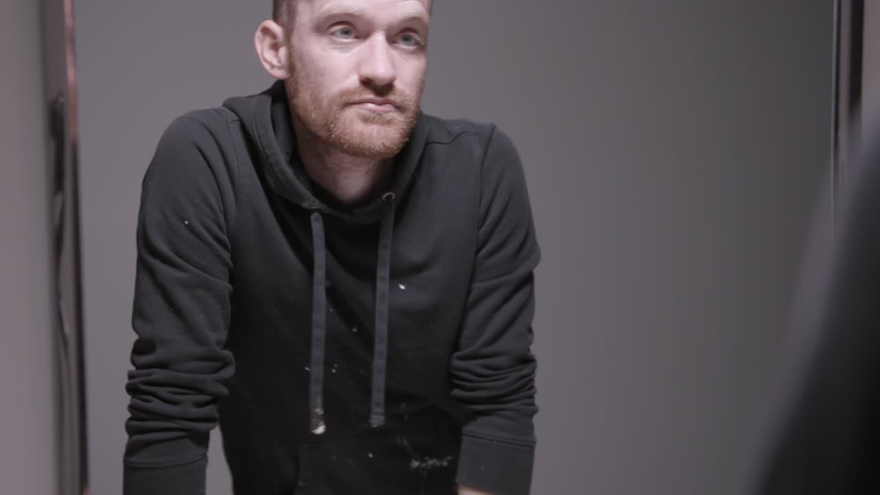 un hombre con una capucha negra salpicando agua en su cara y limpiándola y luego mirándose al espejo con ojos de sufrimiento