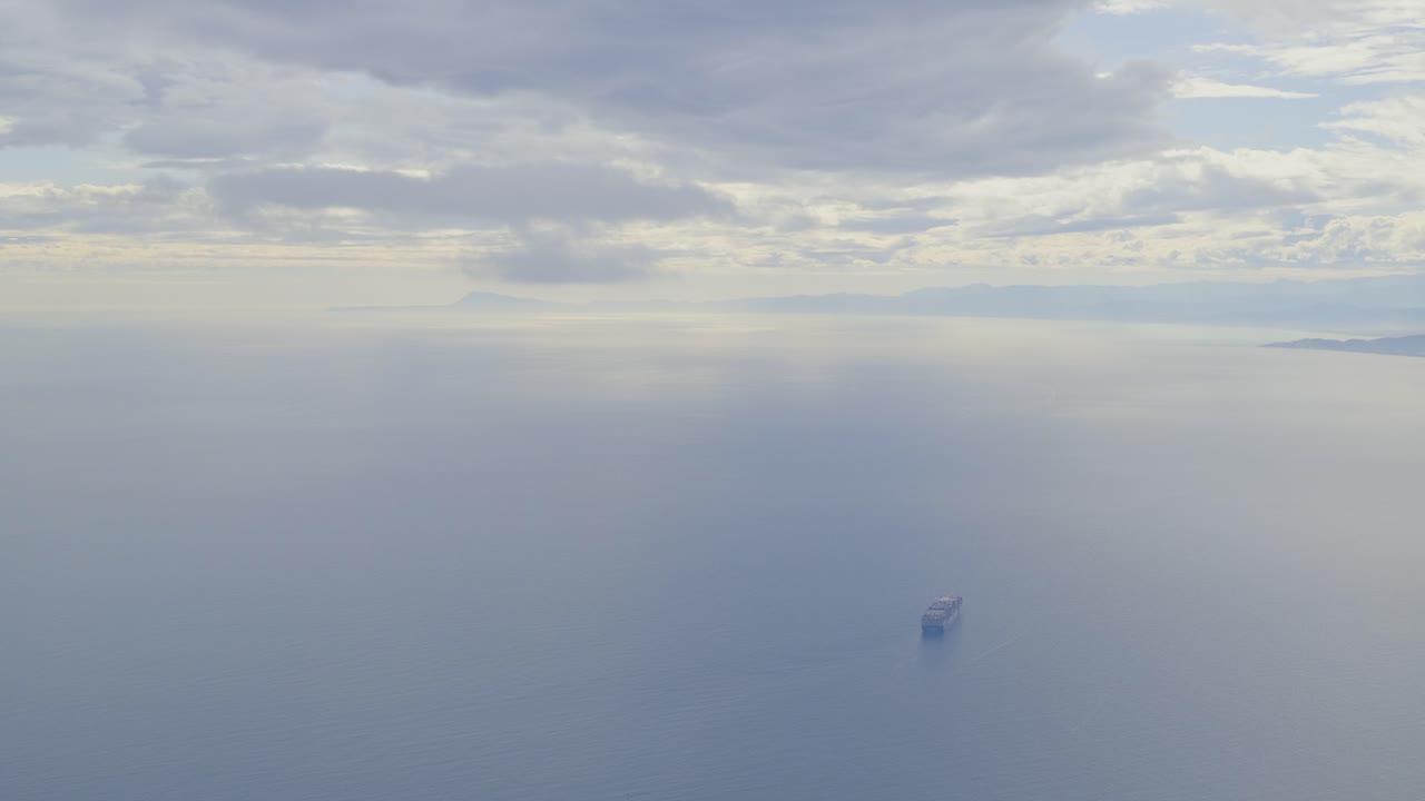 Passenger plane POV of a cargo ship alone at sea under a cloudy sky