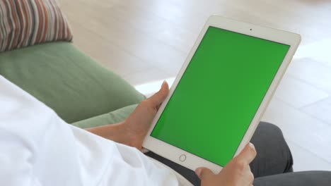punto de vista de la mujer india usando gestos de la mano en pantalla de maqueta verde computadora tableta digital en modo paisaje mientras está sentada en un sofá. en el fondo acogedora sala de estar.