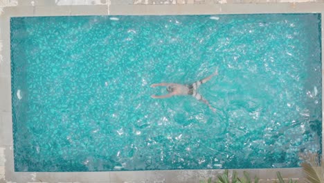 overhead shot of young fit man loose casual swimming trunks breast stroke small private home pool