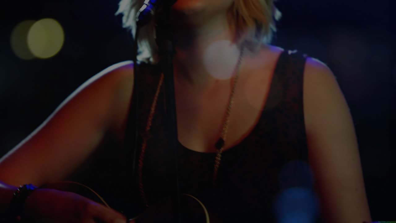 La telecamera si allontana mostrando una cantante adolescente che strimpella e canta nel microfono per uno spettacolo musicale con luci bokeh.