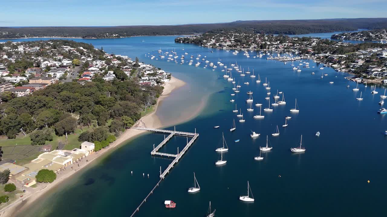 Drone establishing overview of Gunnamatta Bay with boats anchored and houses along the curved shoreline, Sydney NSW Australia