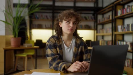 Eine-Studentin-Mit-Lockigem-Haar-Macht-Ein-Aufwärmtraining,-Während-Sie-In-Der-Universitätsbibliothek-An-Einem-Laptop-Arbeitet