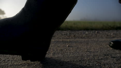 person walking in boots on gravel near a field on a misty morning