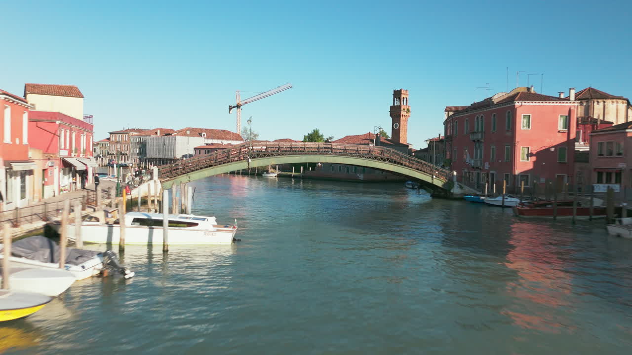 Aerial view of a charming canal in Murano, Venice featuring a historic bridge and a tall clock tower.
