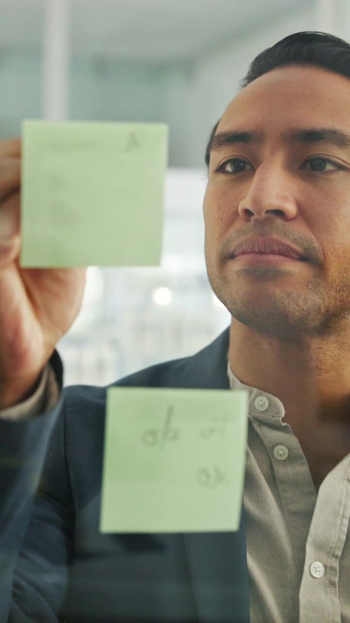 Professional Man Organizing Ideas on Glass Wall with Sticky Notes