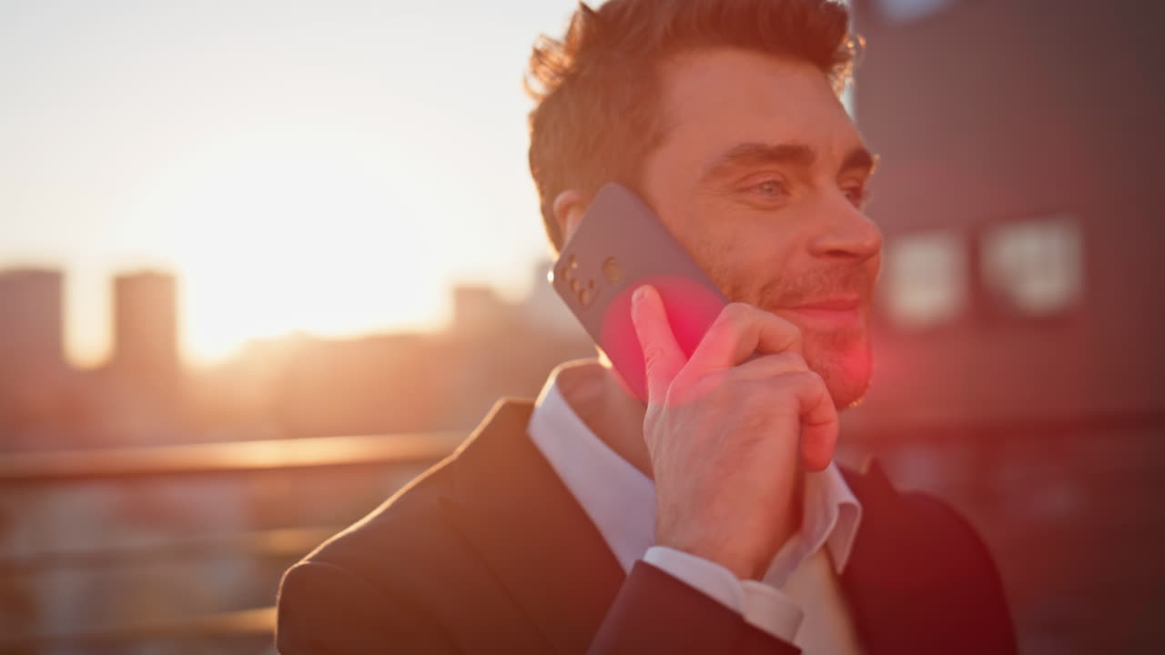 Joyful businessman speaking cellphone standing at sunset rooftop closeup