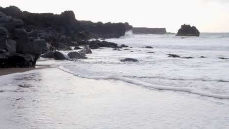 Sanfte-Wellen-Spülen-In-Der-Abenddämmerung-über-Einen-Schwarzen-Sandstrand-Mit-Vulkanischen-Basaltformationen