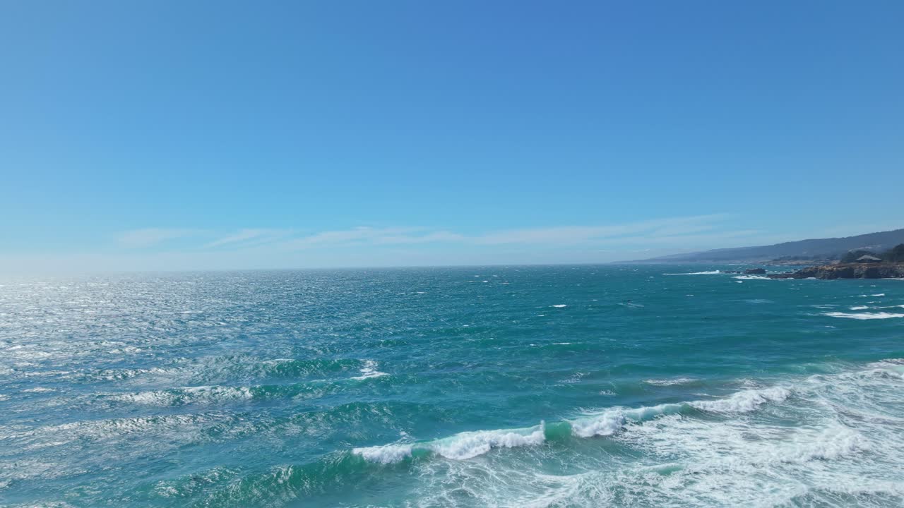 High drone shot capturing powerful waves rolling toward shore under a bright blue sky at Black Point Beach, California