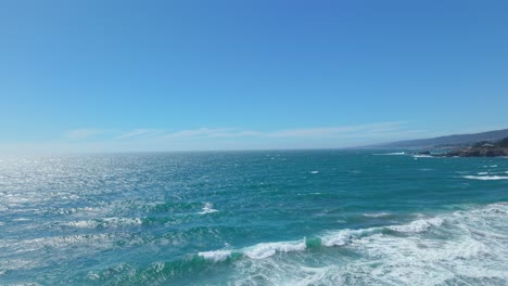 high drone shot capturing powerful waves rolling toward shore under a bright blue sky at black point beach, california