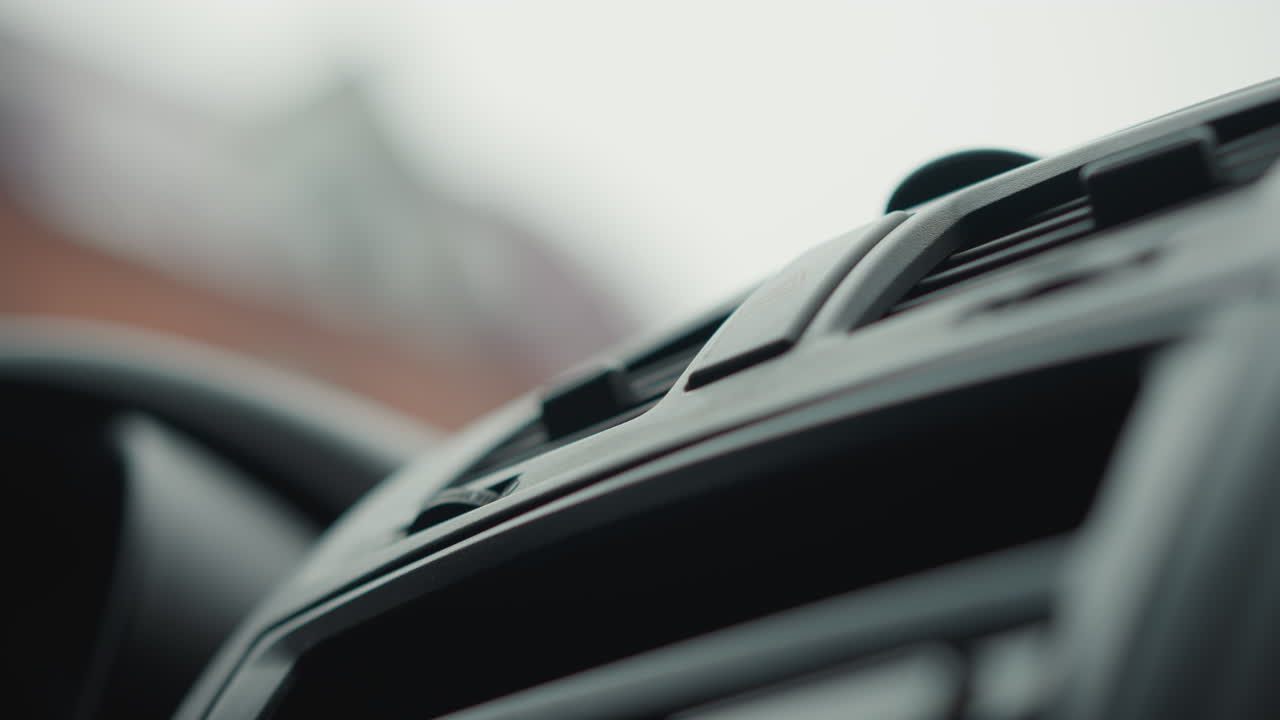 Lower angle view of explorer tapping knob on car dashboard vent control panel under soft cabin lighting highlighting finger gesture, dial texture, slats, ambient glow during winter commute