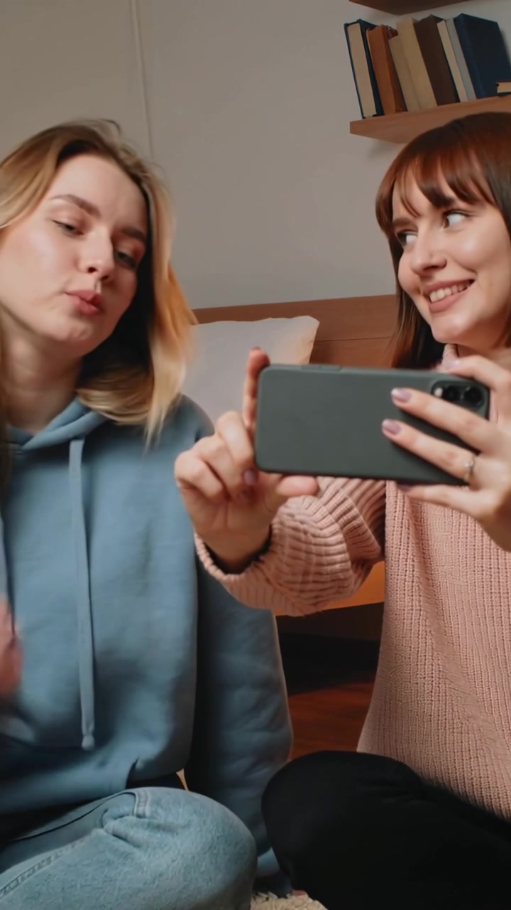 Vídeo vertical: Amigos posando no sofá, vestindo moletom com capuz e suéter de tricô, com telefone sendo segurado para uma selfie.