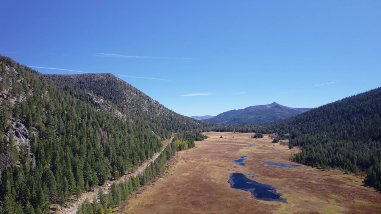 Vista drone di una valle panoramica ad alta quota con pendii boscosi e piccoli specchi d'acqua.