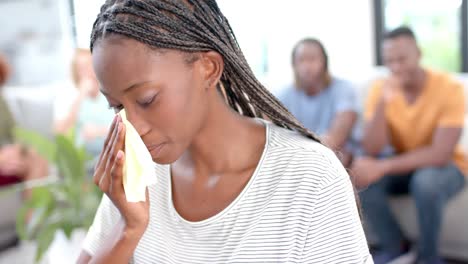 emotional woman crying with diverse friends talking in background during group therapy session