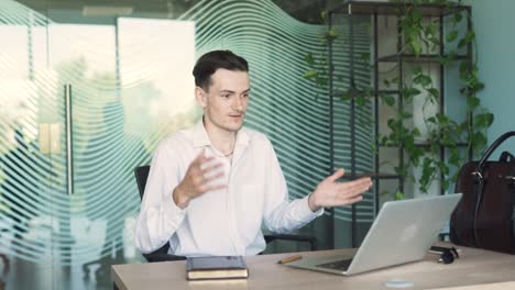 retrato de un hombre guapo, joven y elegante con ropa de negocios, sentado en un escritorio en una oficina moderna, hablando y discutiendo con alguien a través de una llamada de video