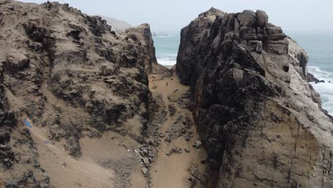 Drohnenvideo-Einer-Person,-Die-Durch-Einen-Bergpass-An-Einem-Felsigen-Strand-Geht