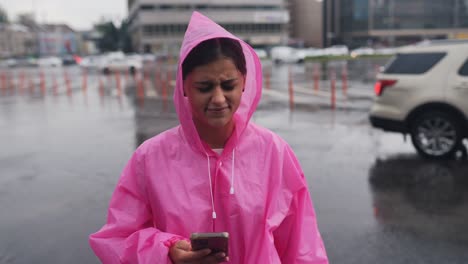 mujer en impermeable rosa usando un teléfono inteligente en la lluvia