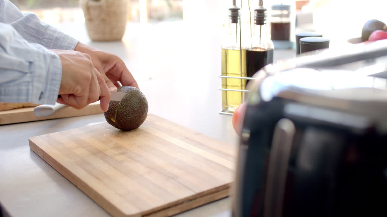 Cutting avocado on wooden board, person preparing healthy meal in kitchen