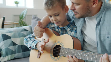 father teaching his son how to play guitar
