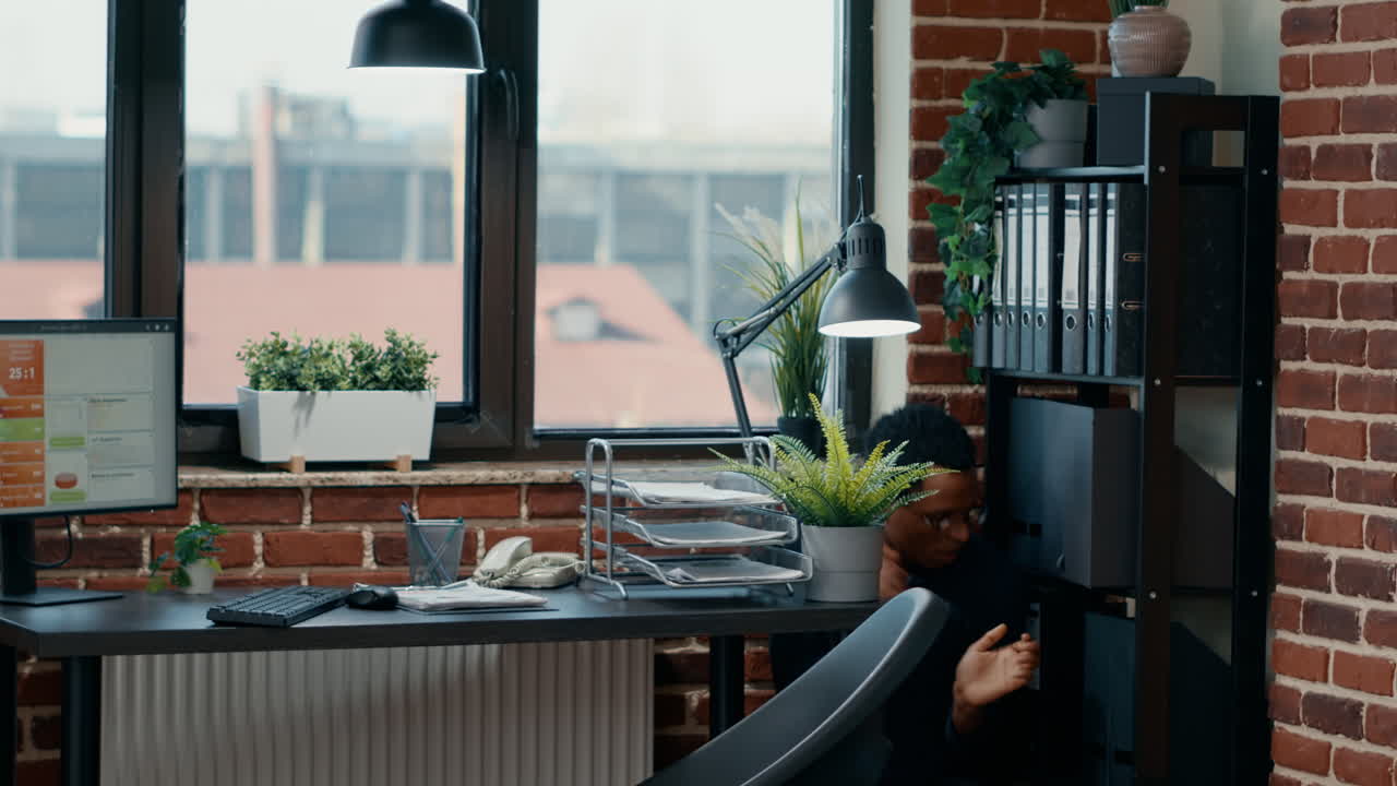 Terrified businessman in office hiding under table from scary zombies