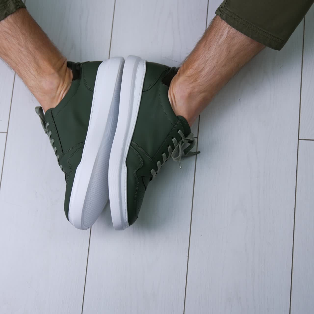 Model sitting on the floor wearing casual sneakers with laces. Man demonstrating stylish footwear at the backdrop of white floor. Top view close up