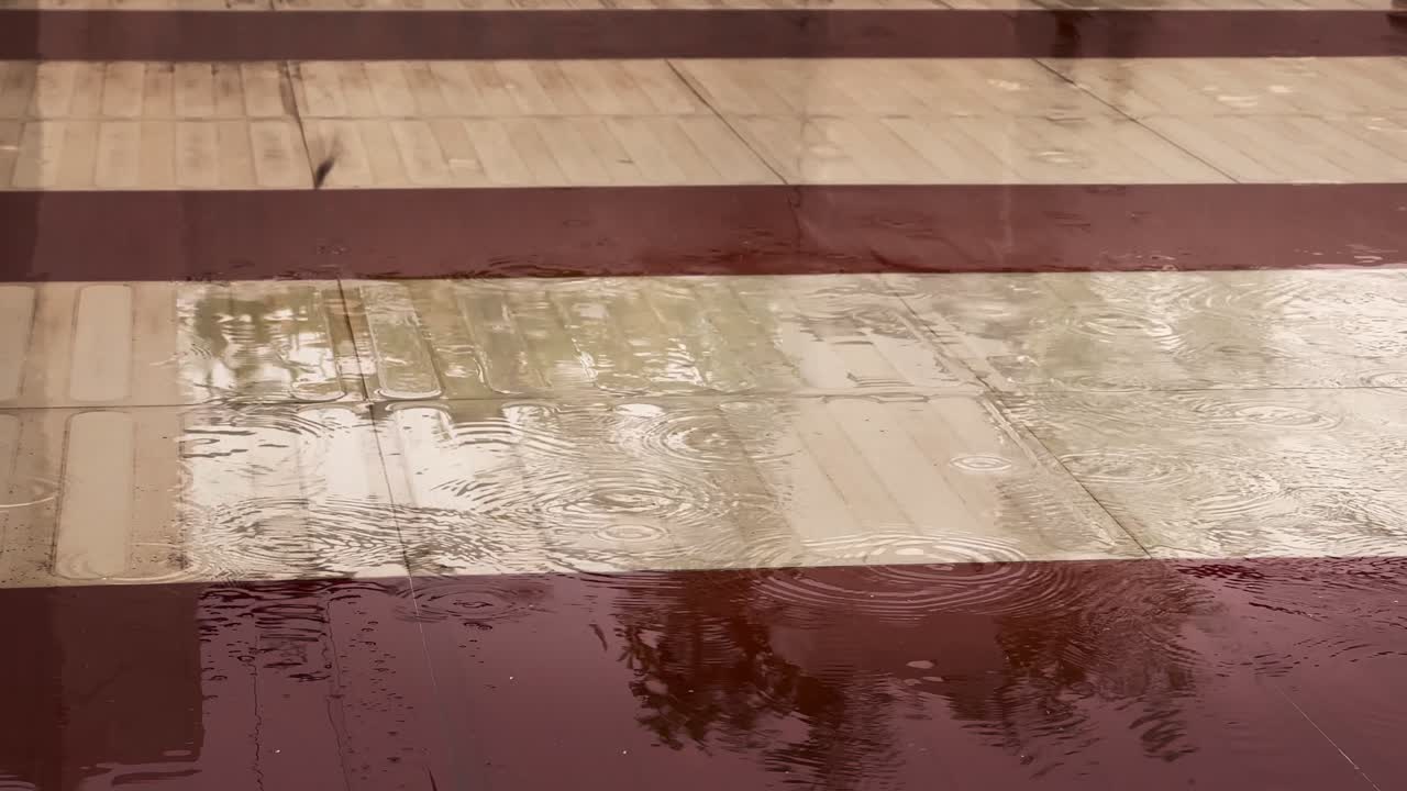 Regn falder på fortovet i slow motion; en regndråbe falder langsomt ned i en vandpyt på jorden.