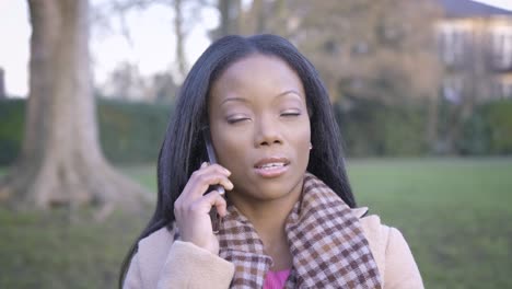 mujer negra confiada hablando por teléfono en el parque