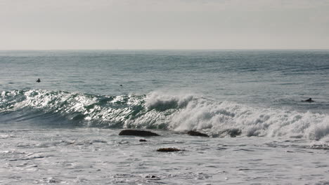 a surfer riding a wave ducks out of a shore break as he gets too close to a patch of rocks in the water