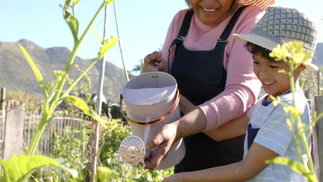 Feliz-Abuela-Birracial-Y-Nieto-Regando-Plantas-En-Un-Jardín-Soleado,-Cámara-Lenta