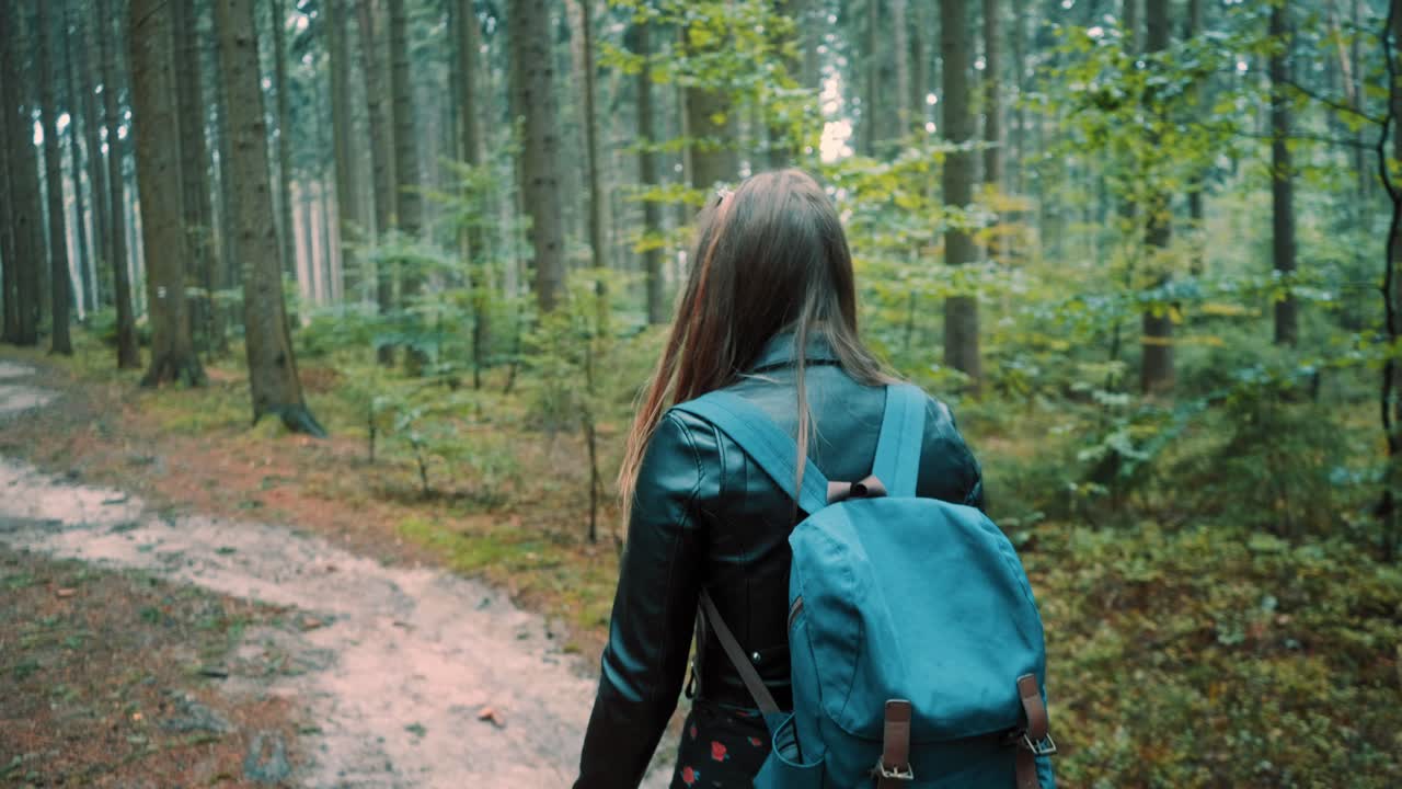 Girl with long beautiful hair is walking along a forest path with a backpack