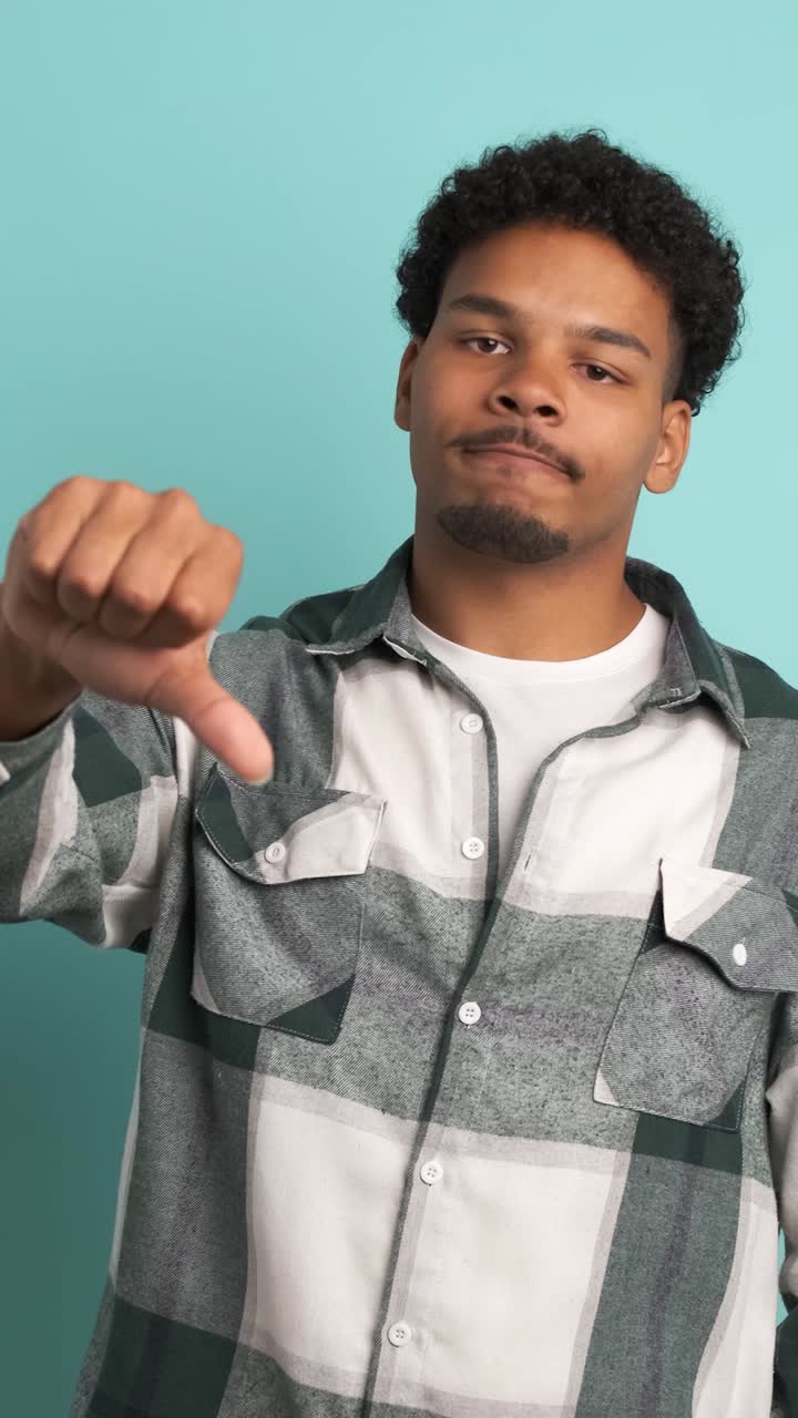 Sad young man showing thumb down in blue studio