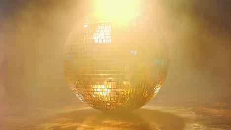 a large gold disco ball sits on a sandy surface. the ball is surrounded by a hazy, smoky atmosphere, giving the impression of a dimly lit dance floor