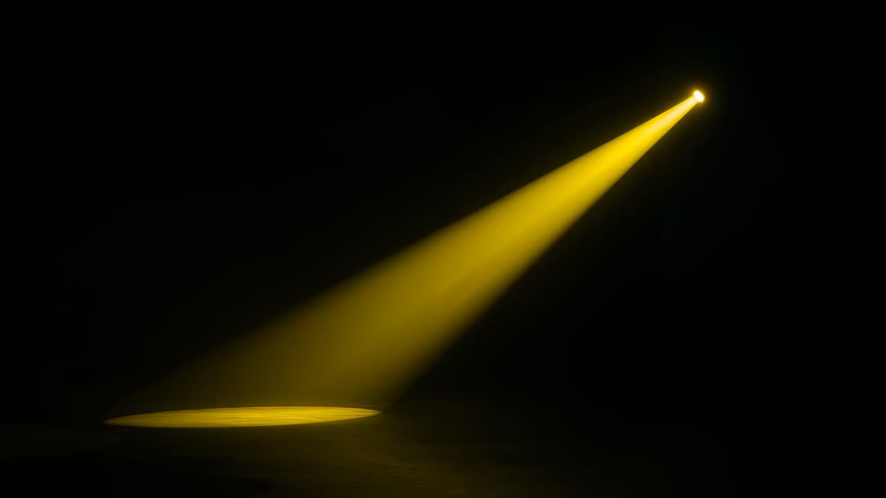 Lysende spotlight, der projicerer en enkelt gul stråle, som udvides på et mørkt scene gulv og reflekterer