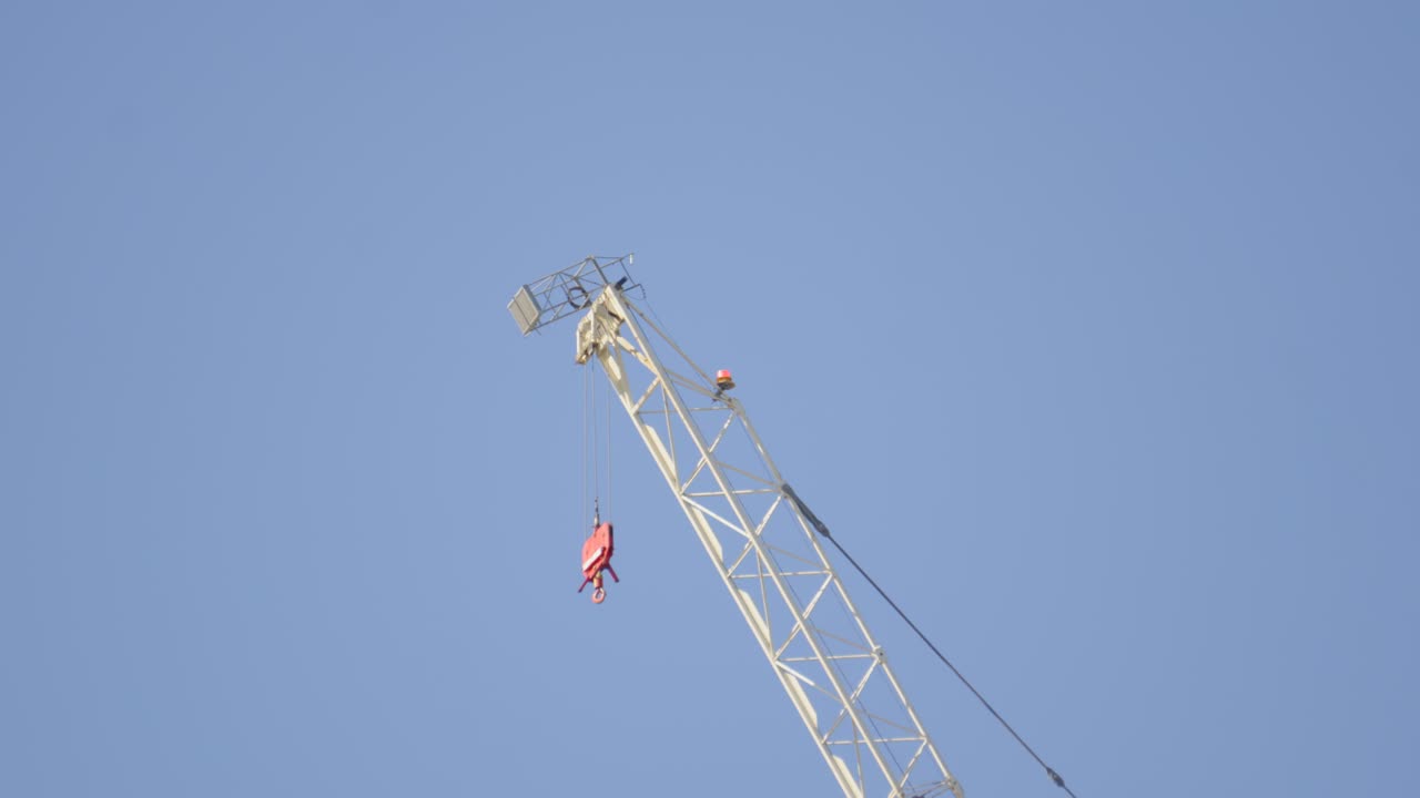 Top of Tower Crane with Wire and Hook. Industrial Machinery Used for Building Construction. Symbolizes heavy lifting, logistics, and progress. Filmed in UK