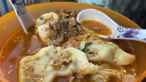 very close up shot over steamed momo in spicy soup served in a yellow bowl at a roadside stall