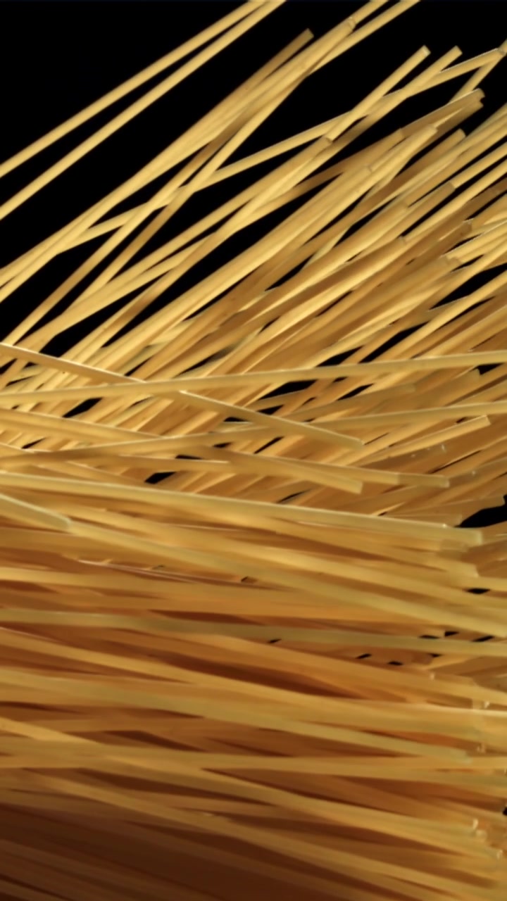 Spaghetti dorati che cadono e si disperdono su sfondo nero