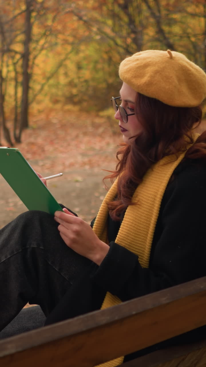 vista lateral de la artista sentada en un bosque sereno, profundamente enfocada en dibujar en su libro, rodeada de colores de otoño y un entorno al aire libre tranquilo
