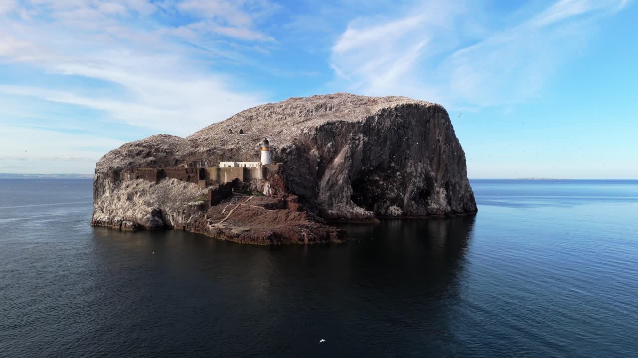 Aerial drone footage of Bass Rock, an island off the coast of North Berwick, Scotland, in the warm summer sunshine. North Sea, rugged cliffs, seabird colonies.