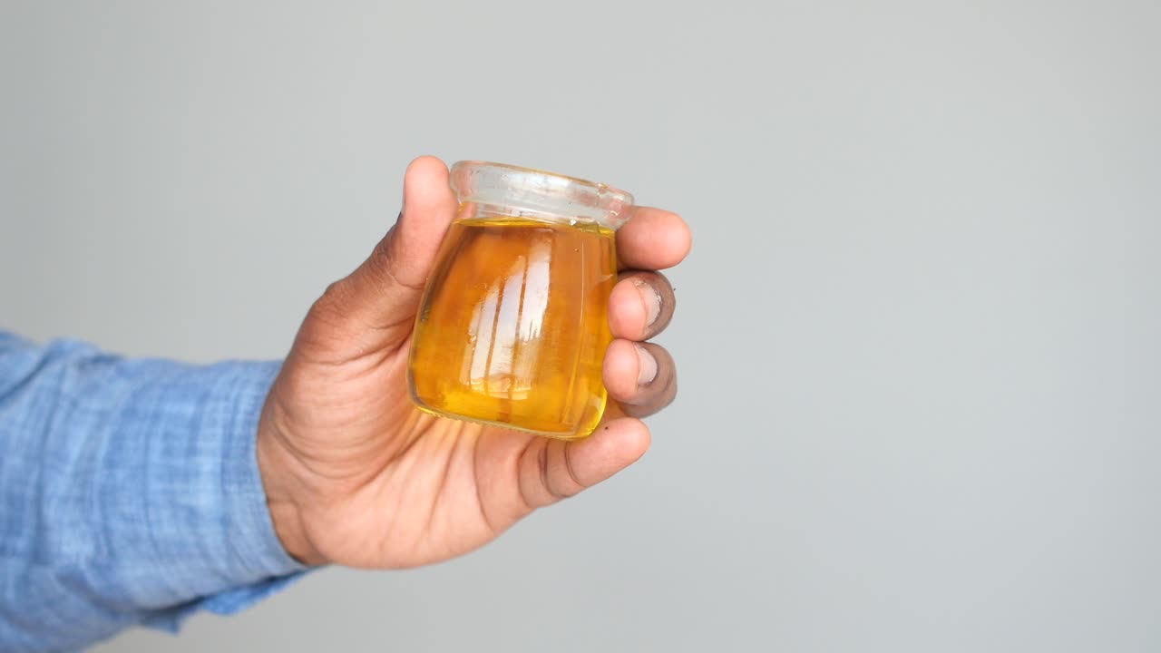Hand holding a small glass jar filled with yellow liquid