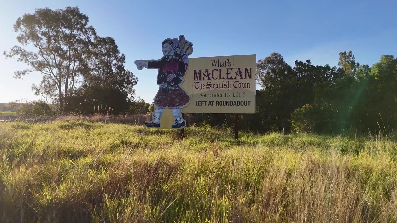 Ampia inquadratura statica di un cartello di benvenuto a bordo strada e di una sagoma di suonatore di cornamusa a Maclean, Australia