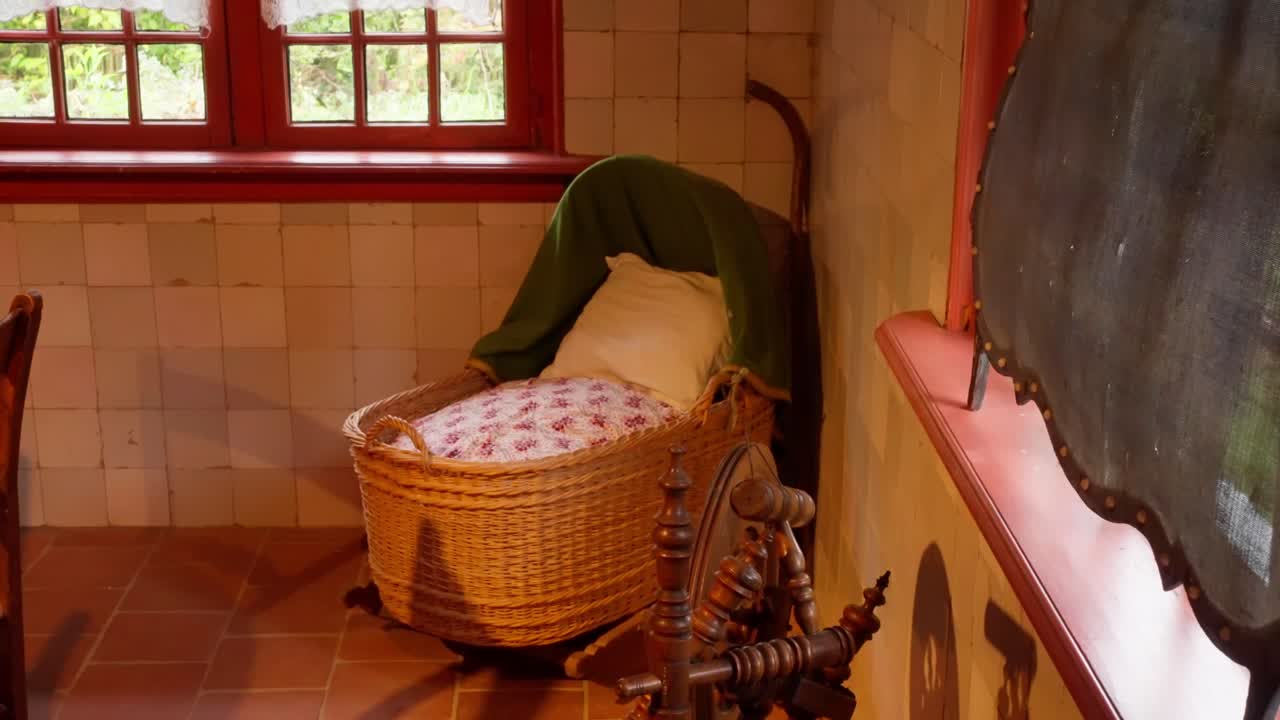 Antique wicker baby crib and wooden spinning wheel in a historic room setting. Traditional Dutch interior with red window frames and white tiled walls