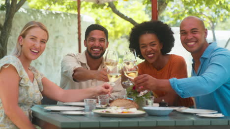 portrait of group of friends enjoying outdoor meal and wine on visit to vineyard restaurant