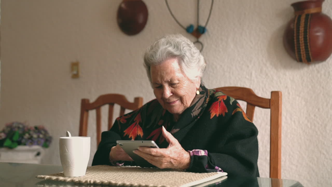Aged woman with gadget sitting at table
