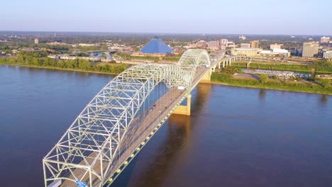 Magnífica-Antena-Acercándose-A-Memphis,-Tennessee,-Cruzando-El-Río-Mississippi-Con-El-Puente-Hernando-De-Soto-En-Primer-Plano-Y-El-Fondo-De-La-Pirámide-De-Memphis