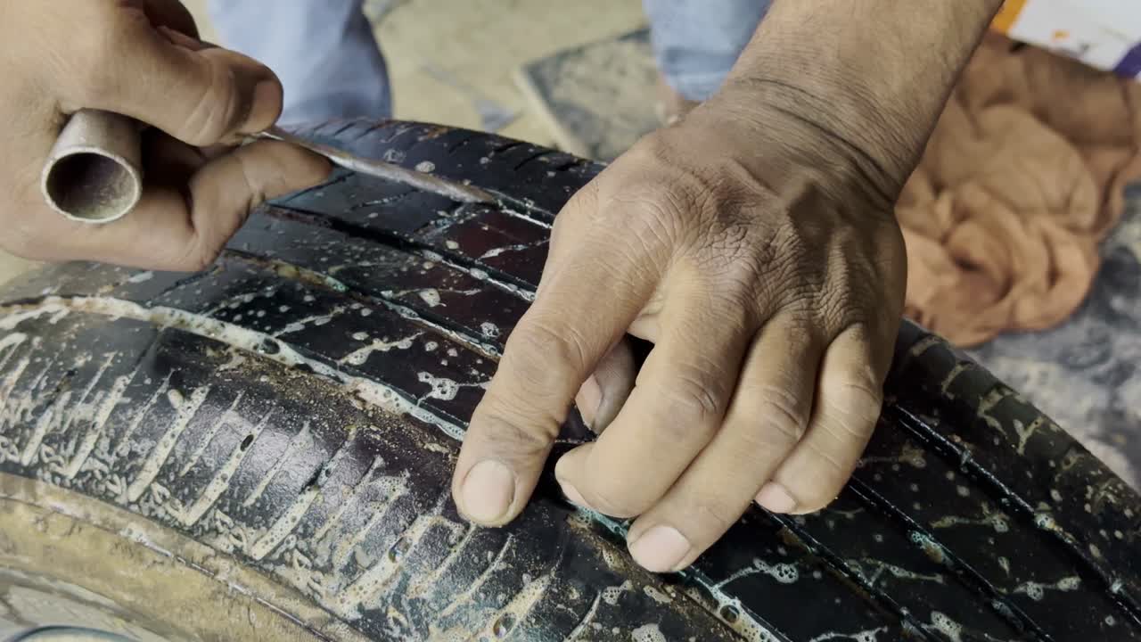 Close-up static shot of a mechanic checking a punctured tire using soap water method to find air bubbles
