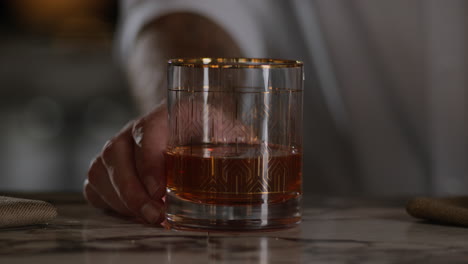 bartender places his hand on an unfinished old fashioned cocktail