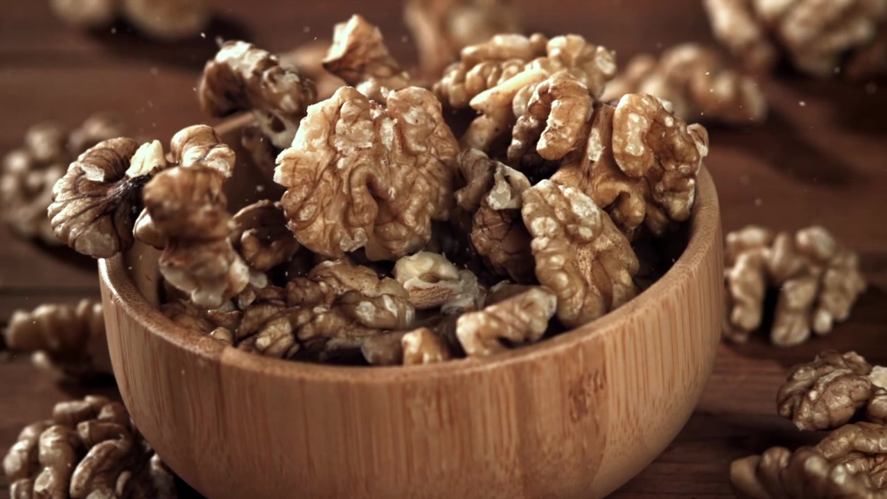 Shelled Walnuts Falling into a Wooden Bowl in Slow Motion