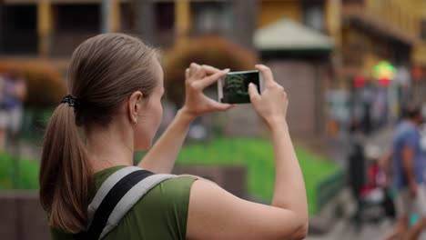 una mujer joven en un viaje tiene a su bebé en una mochila de canguro y usa un teléfono móvil para tomar fotos. mientras camina, revisa la pantalla periódicamente