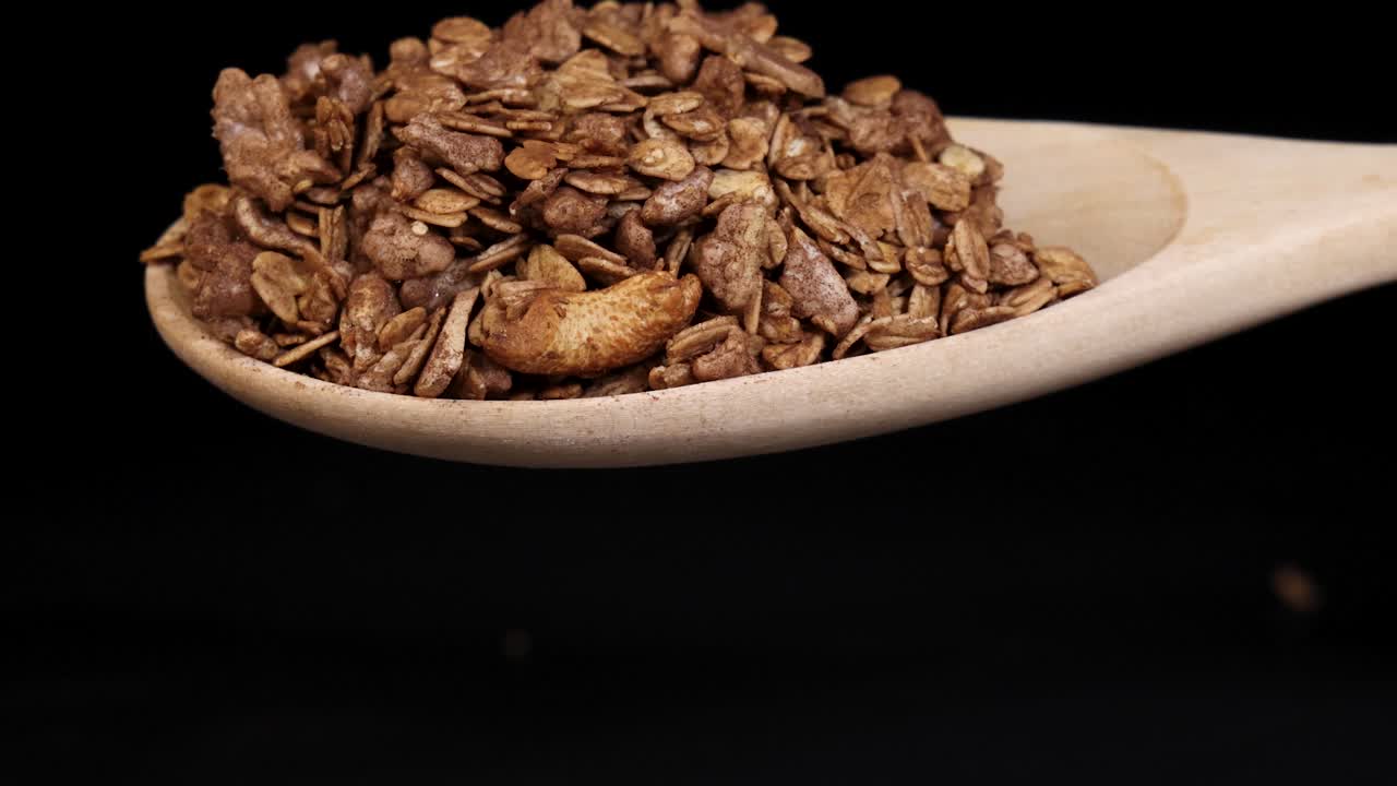 Granola pouring from wooden spoon on black background